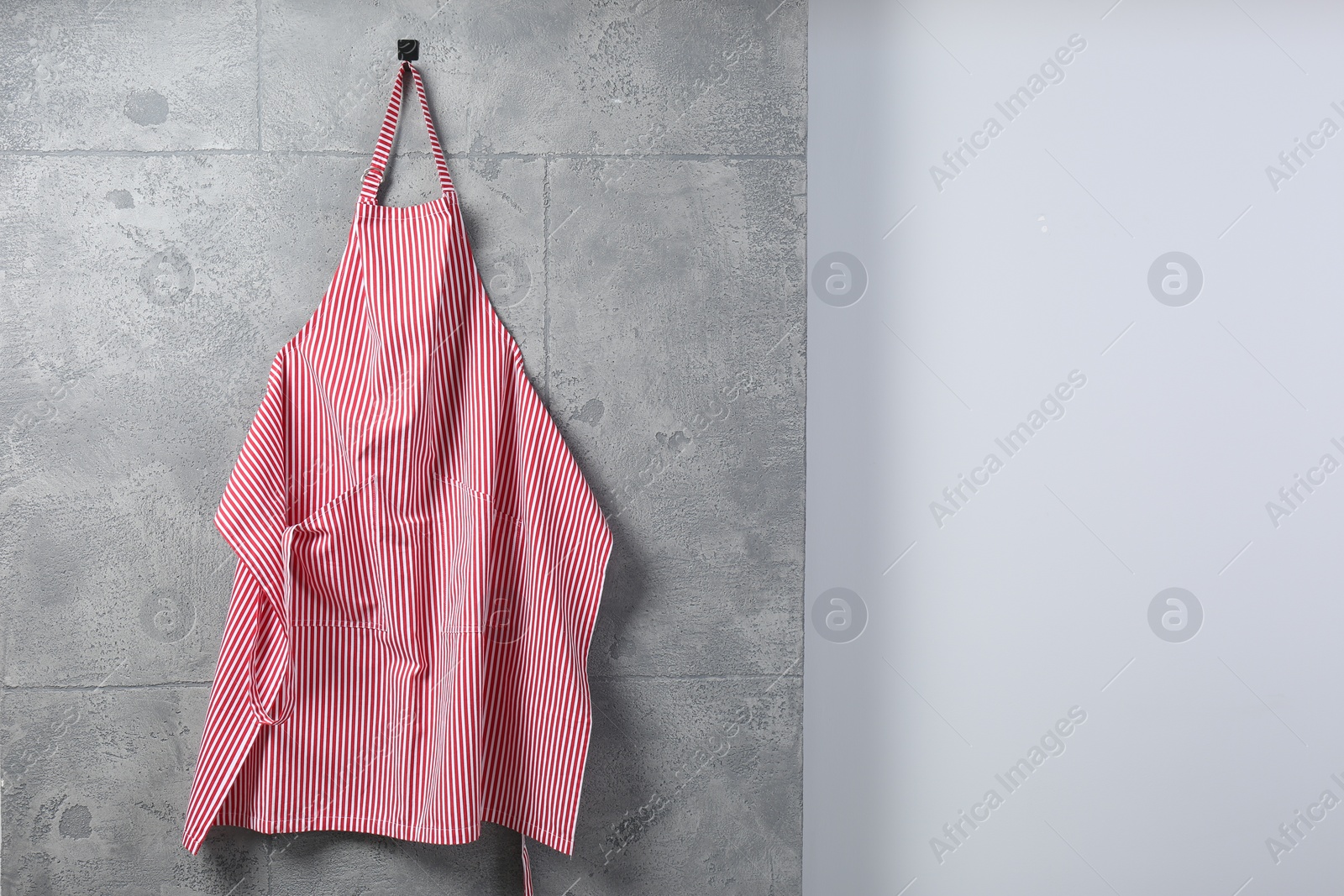 Photo of Clean red striped apron on grey tiled wall. Space for text