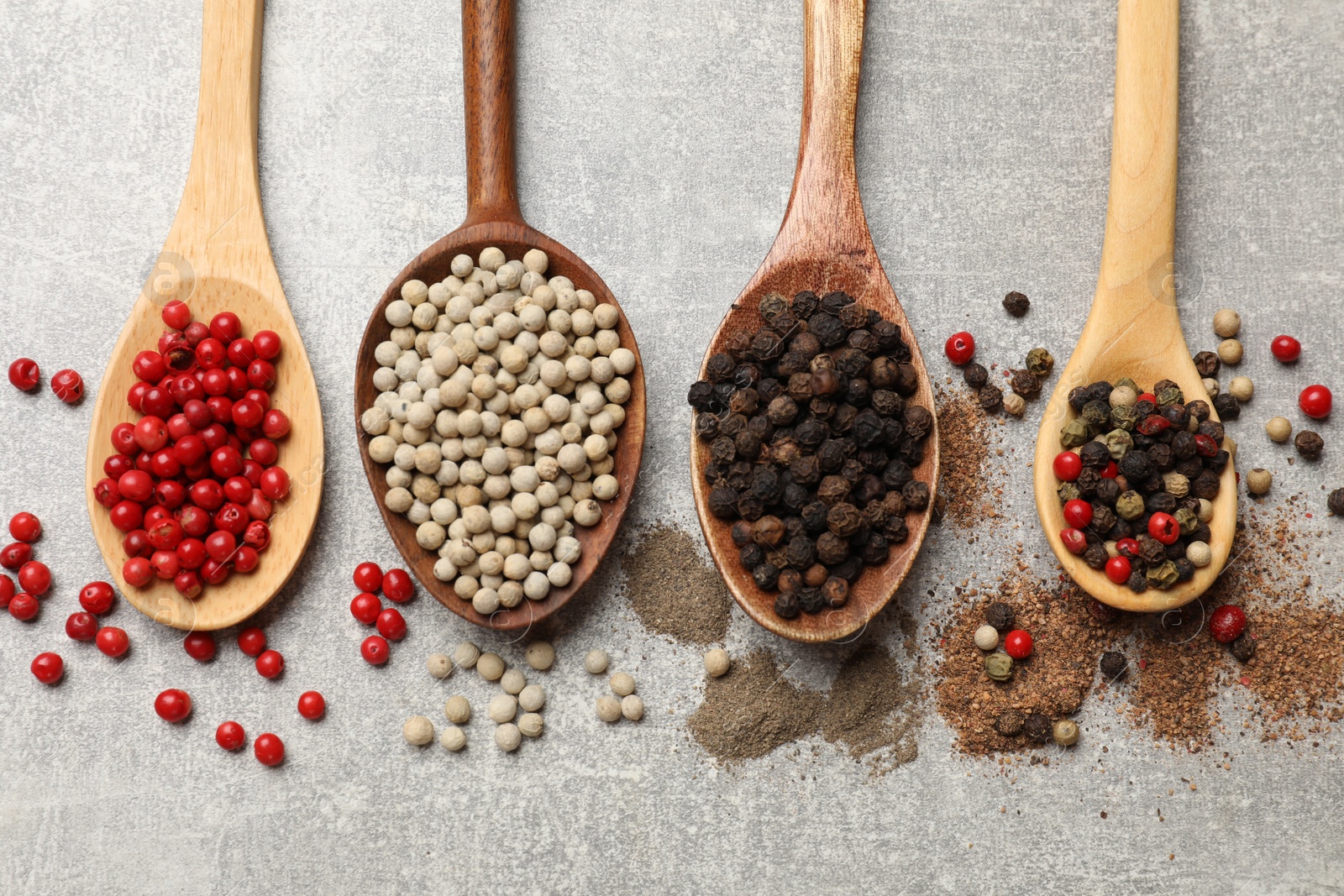 Photo of Aromatic spice. Different peppers in spoons on light textured table, flat lay