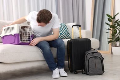 Photo of Travel with pet. Man closing carrier with cat on sofa at home