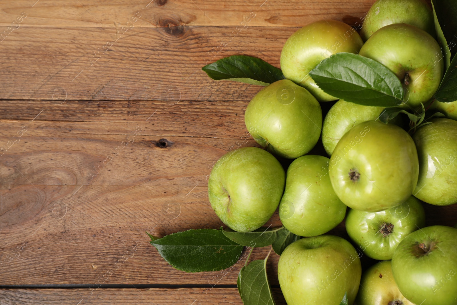 Photo of Ripe green apples with leaves on wooden table, flat lay. Space for text