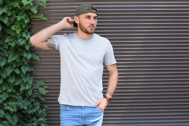 Young man wearing gray t-shirt near wall on street. Urban style