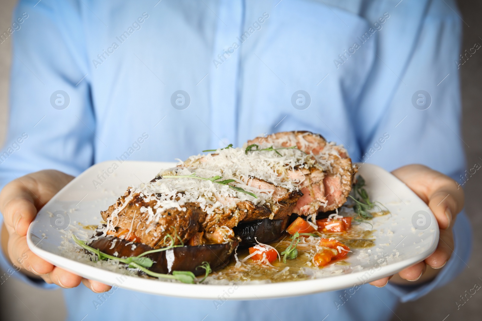 Photo of Woman holding plate with delicious roasted meat on grey background, closeup