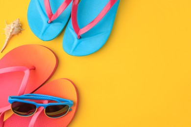 Flip flops and sunglasses on yellow background, flat lay with space for text. Beach accessories