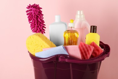 Photo of Bucket with different cleaning supplies against pink background, closeup