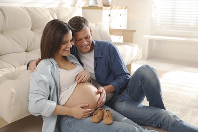 Young pregnant woman and her husband with baby's shoes at home