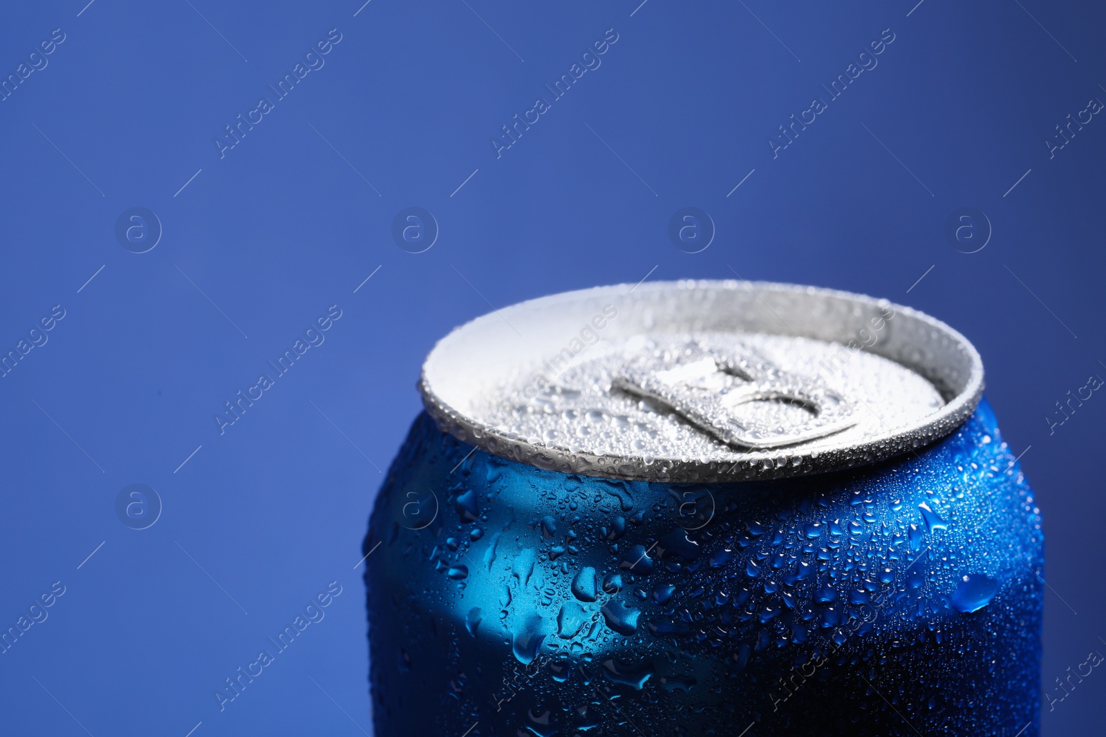 Photo of Aluminum can of beverage covered with water drops on blue background, closeup. Space for text