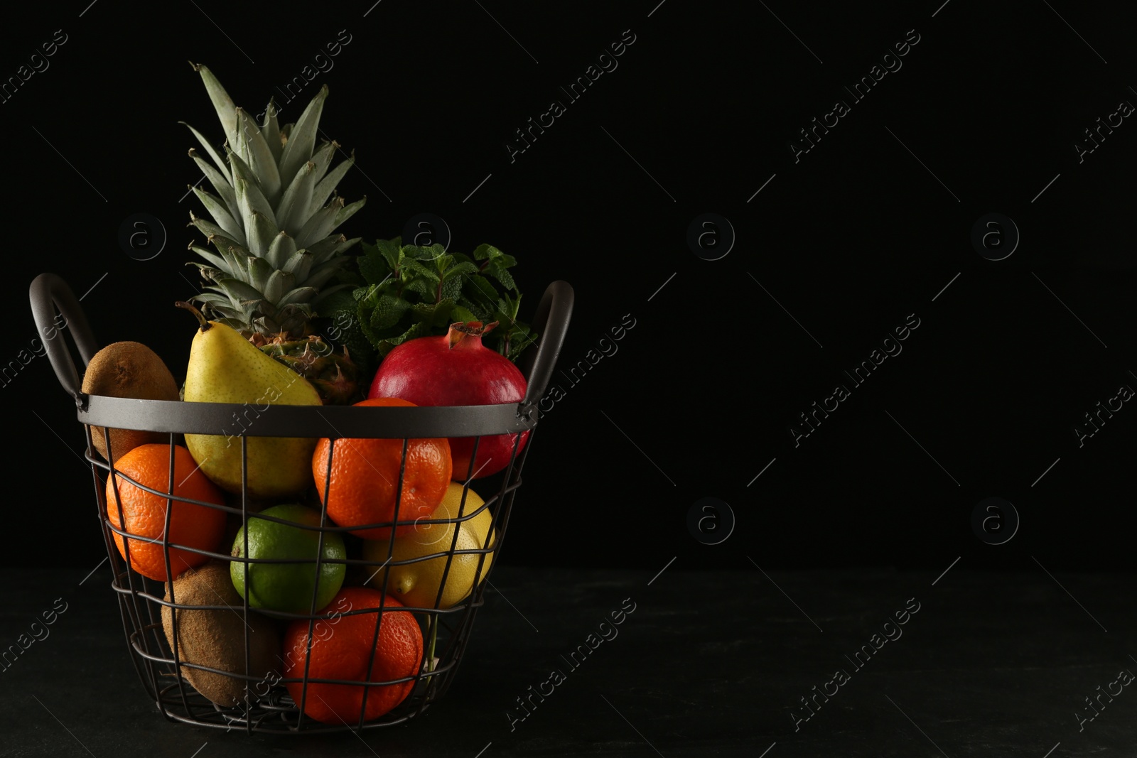 Photo of Fresh ripe fruits in metal basket on black table, space for text