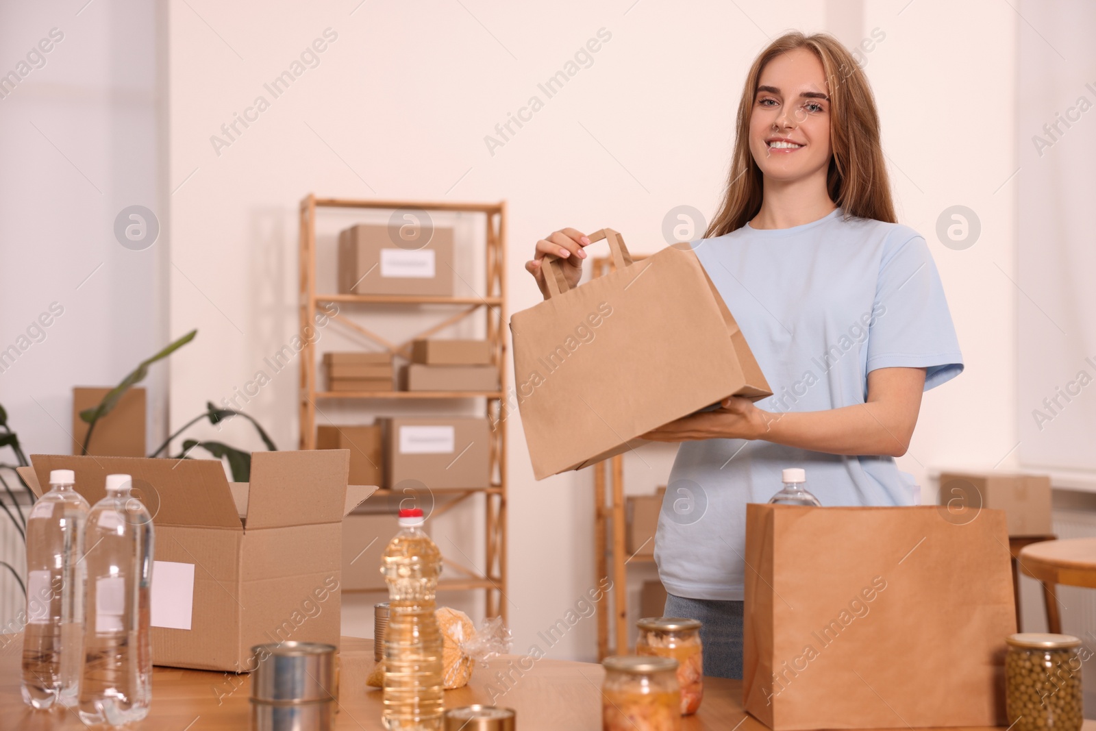 Photo of Volunteer with paper bag and food products on table in warehouse