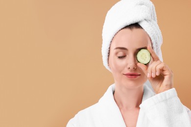 Photo of Beautiful woman covering eye with piece of cucumber on beige background, space for text