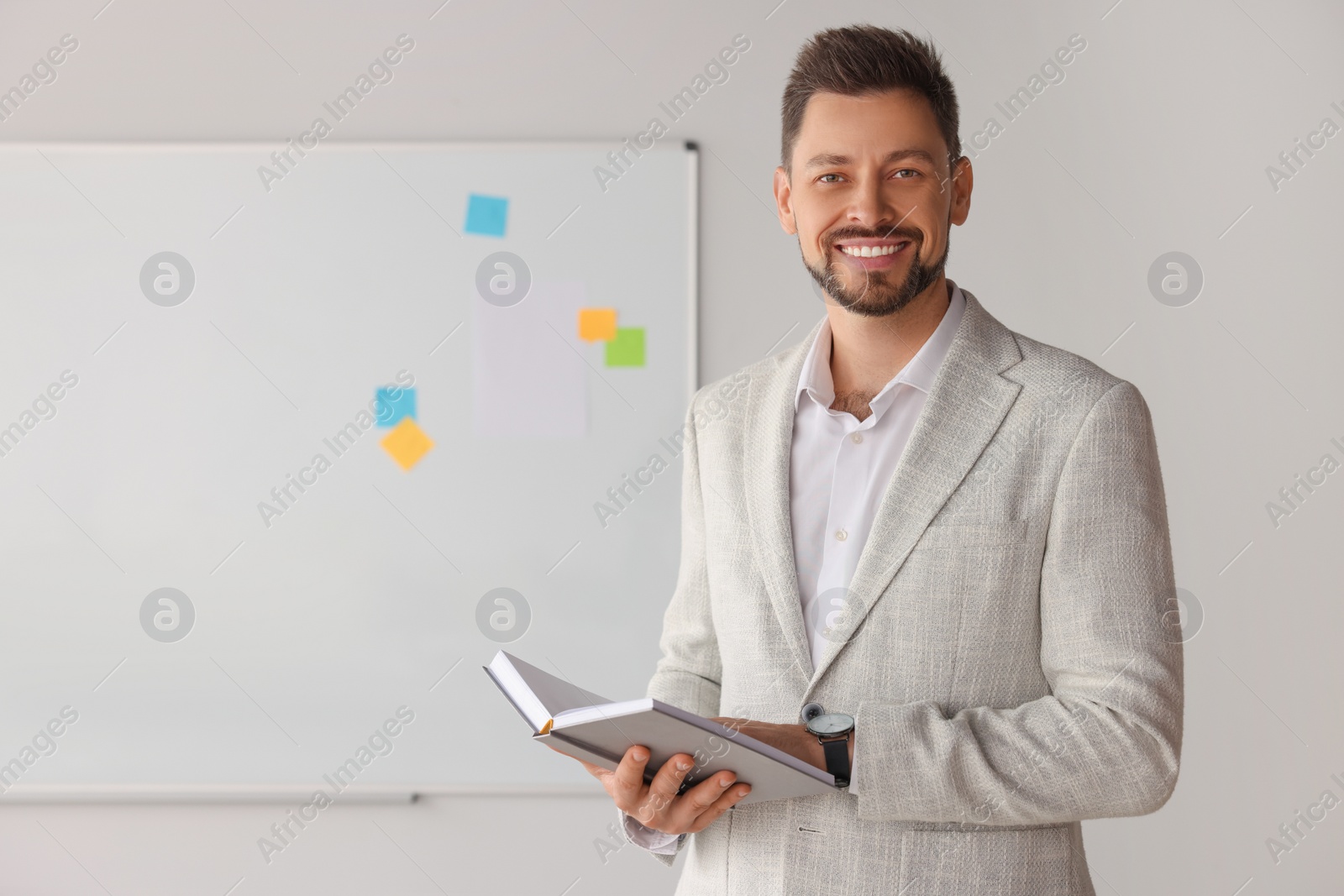 Photo of Happy teacher with book at whiteboard in classroom
