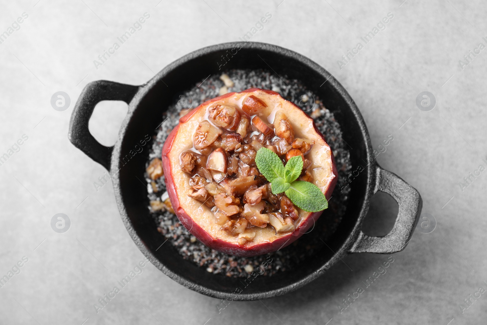 Photo of Tasty baked apple with nuts, honey and mint in baking dish on gray table, top view