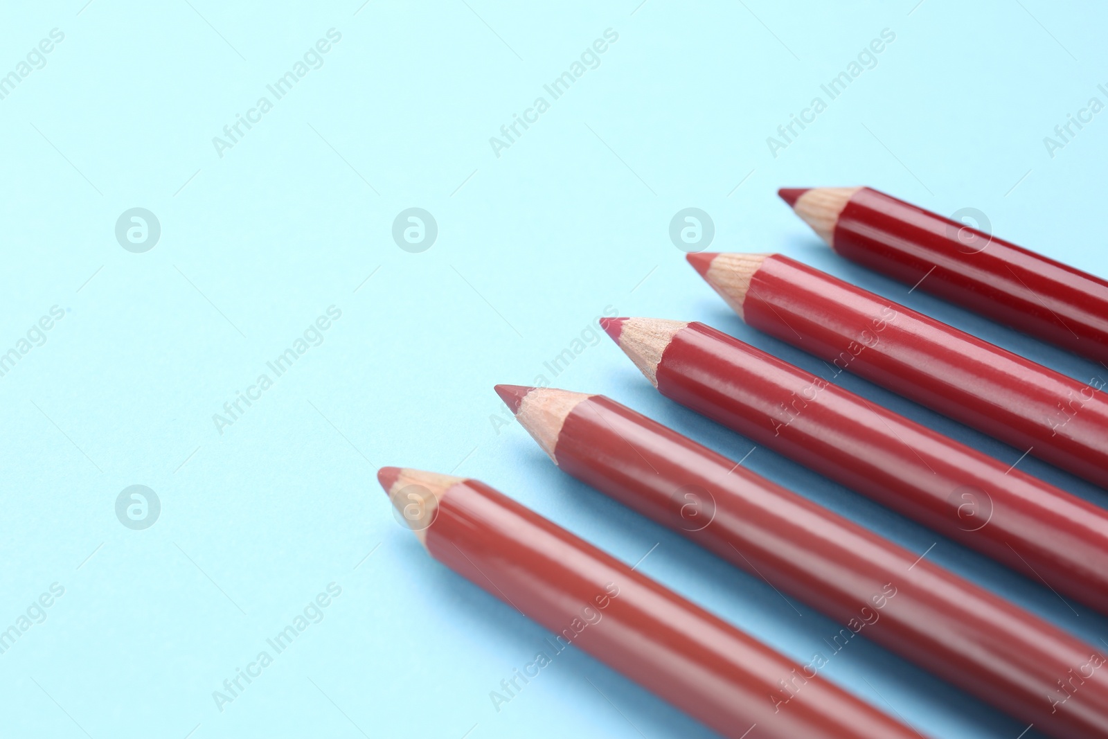 Photo of Different lip pencils on light blue background, closeup view with space for text. Cosmetic product