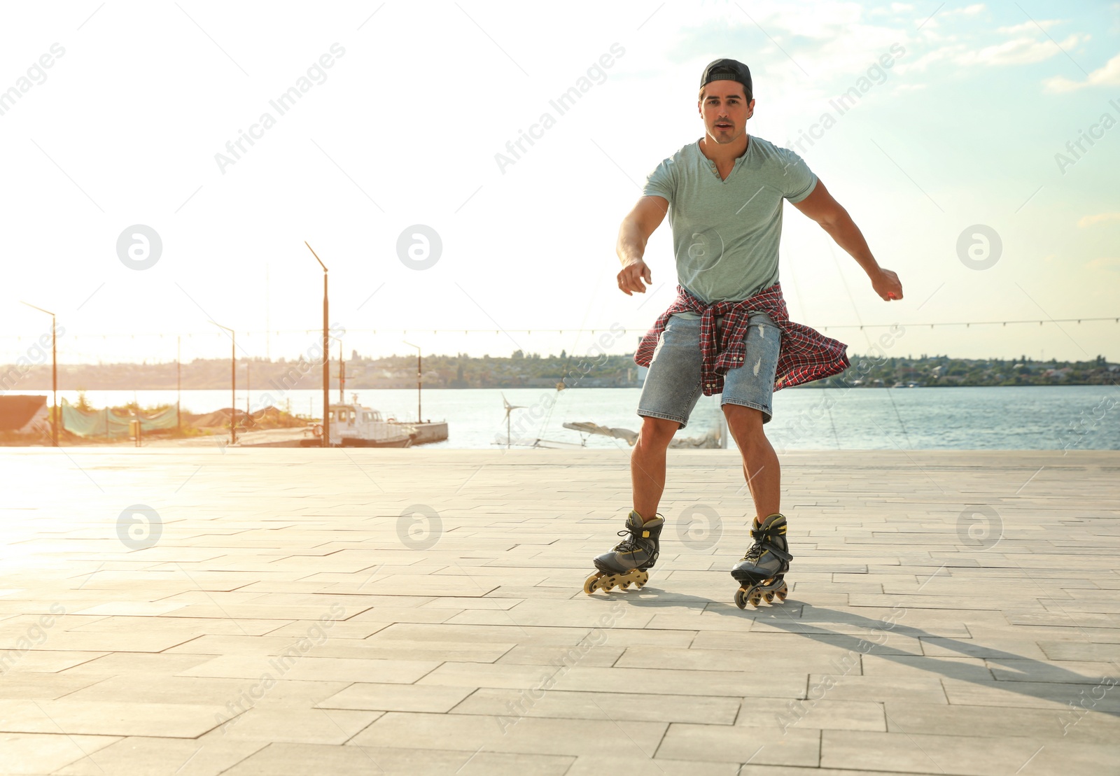 Photo of Handsome young man roller skating on pier near river, space for text