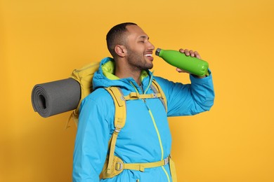 Photo of Happy tourist with backpack drinking on yellow background