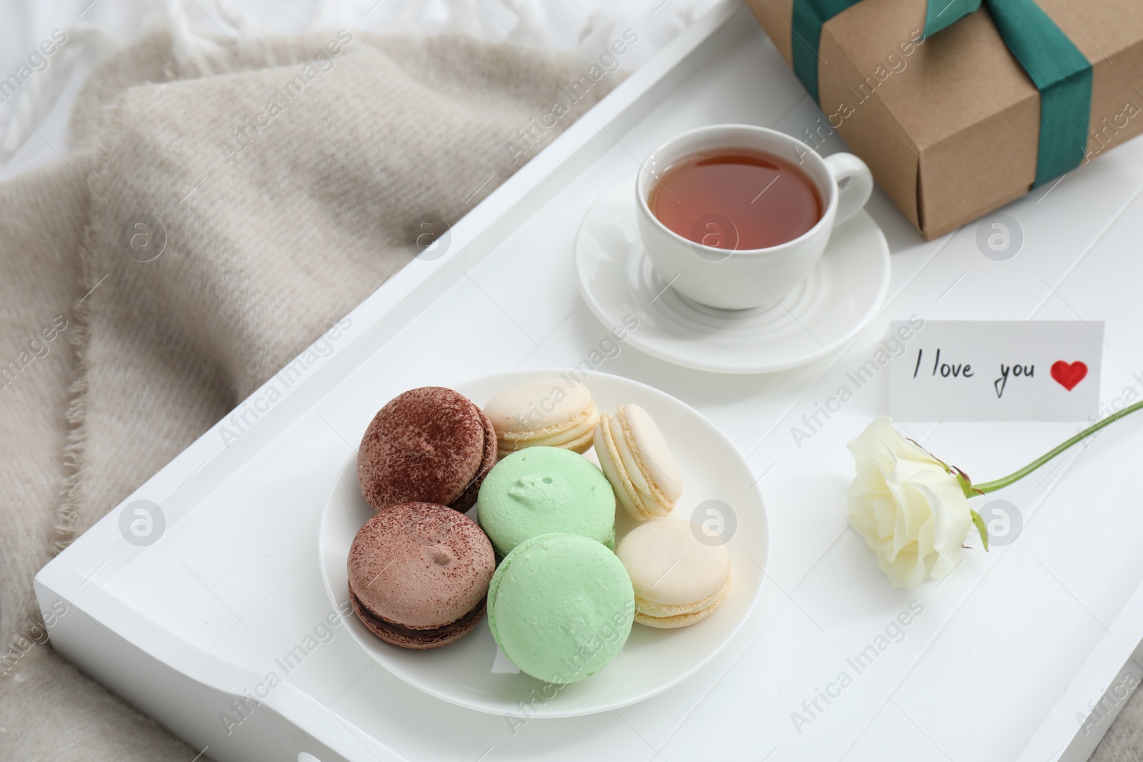 Photo of Tasty breakfast served in bed. Delicious macarons, tea, gift box, rose and I Love You card on tray