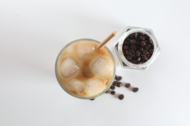 Iced coffee with milk in glass and jar of roasted beans on white background, top view