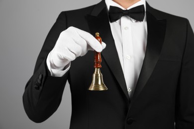 Photo of Butler holding hand bell on grey background, closeup