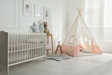 Photo of Comfortable crib and play tent in baby room. Interior design