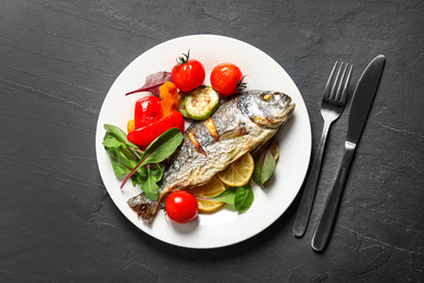 Photo of Delicious roasted fish with lemon and vegetables on dark grey table, flat lay