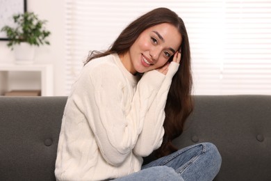 Photo of Beautiful young woman in stylish warm sweater on sofa at home