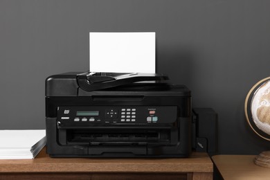 Modern printer with paper on wooden desk at home