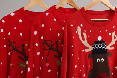 Different Christmas sweaters hanging on rack against light background, closeup