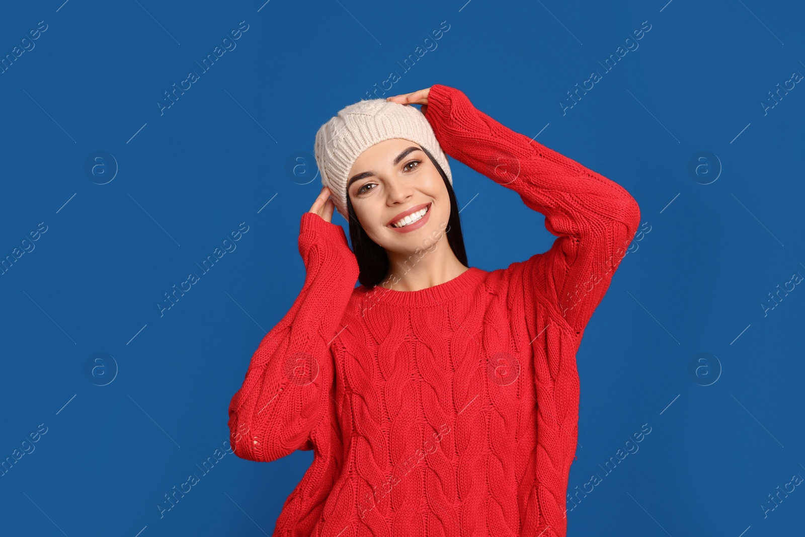 Photo of Young woman wearing warm sweater and hat on blue background. Winter season