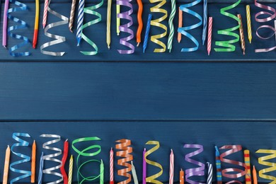 Colorful serpentine streamers and candles on blue wooden table, flat lay. Space for text