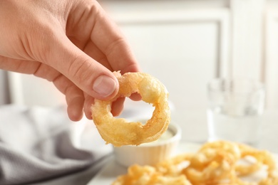 Woman holding homemade crispy onion ring over table, closeup