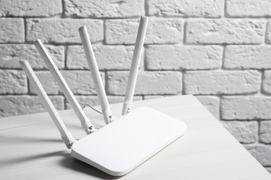 Photo of New Wi-Fi router on white wooden table against brick wall. Space for text
