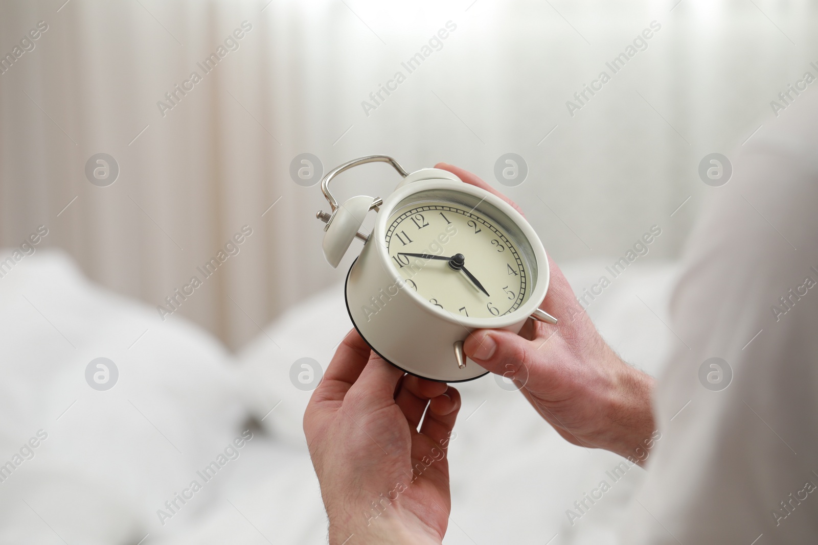 Photo of Man with alarm clock in bedroom, closeup of hands. Space for text