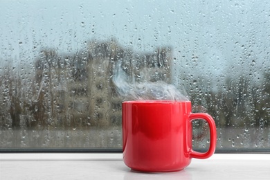 Cup of hot drink on white windowsill. Rainy weather