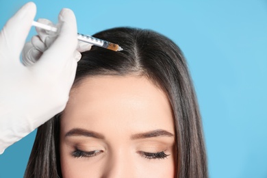 Young woman with hair loss problem receiving injection on color background, closeup