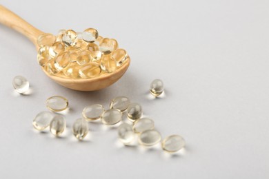 Spoon with vitamin capsules on light background, closeup. Space for text