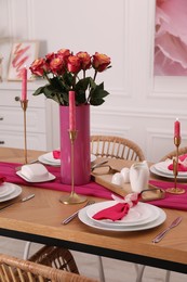 Color accent table setting. Plates, cutlery, pink napkins and vase with beautiful roses in dining room