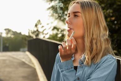 Photo of Young woman smoking cigarette outdoors, space for text