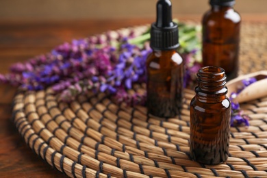 Bottles of sage essential oil and flowers on table, space for text