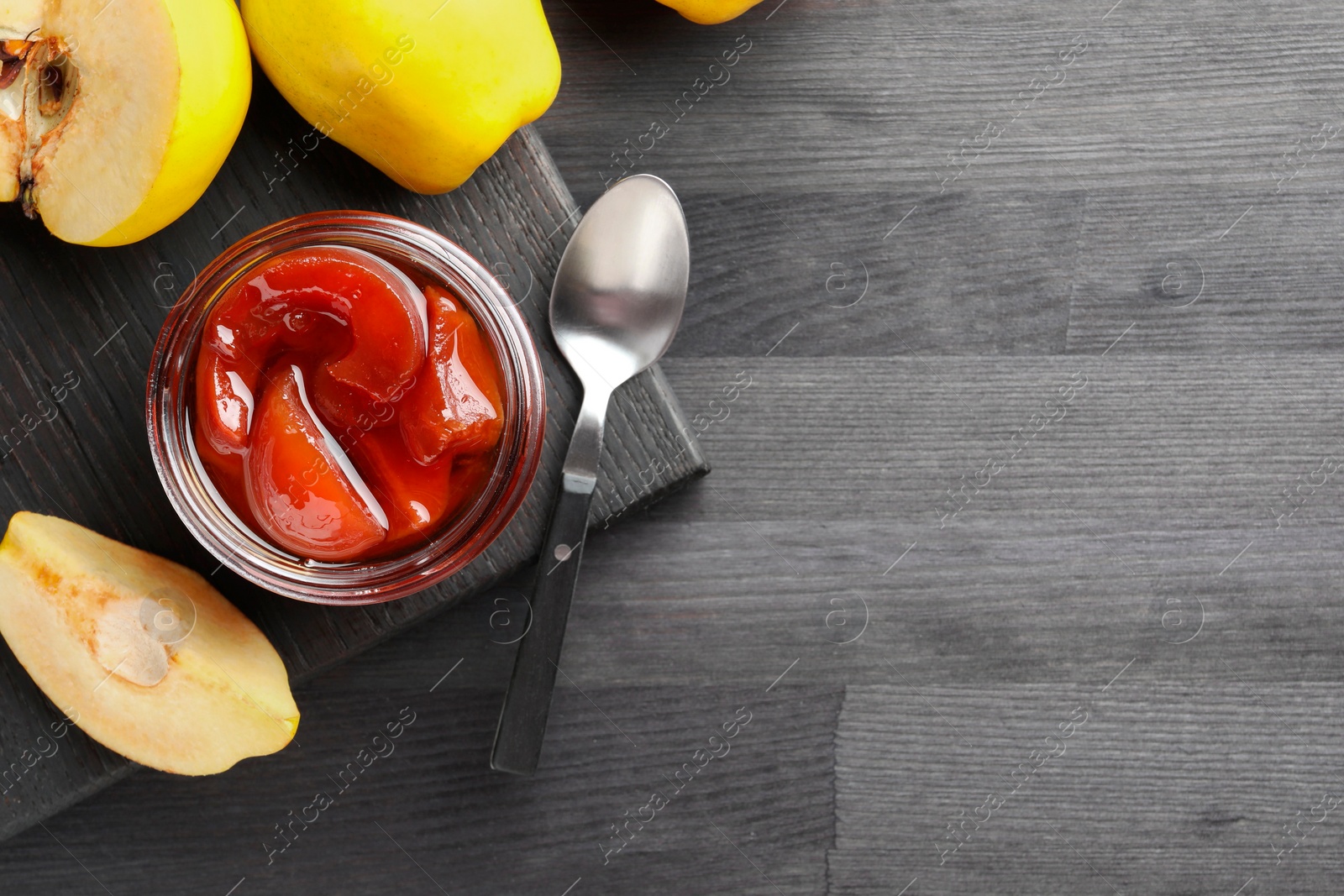 Photo of Quince jam in glass jar, spoon and fresh raw fruits on grey wooden table, flat lay. Space for text