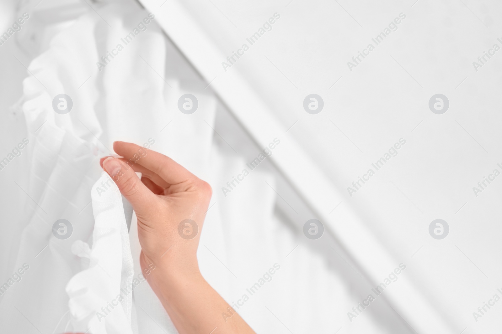 Photo of Young woman hanging window curtain in room, closeup. Space for text