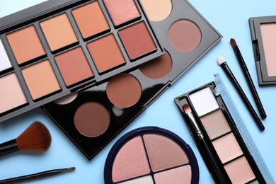 Different contouring palettes and brushes on light blue background, flat lay. Professional cosmetic product