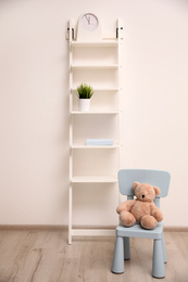 Photo of Teddy bear on chair and shelving unit near wall in child room