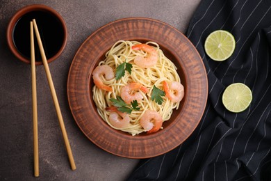 Photo of Tasty spaghetti with shrimps, parsley, lime and soy sauce on brown table, flat lay