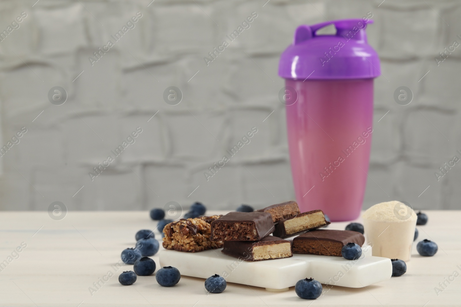 Photo of Different energy bars, blueberries, protein cocktail and powder on white wooden table