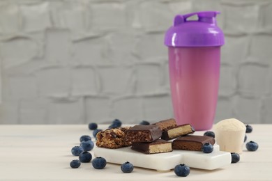Different energy bars, blueberries, protein cocktail and powder on white wooden table