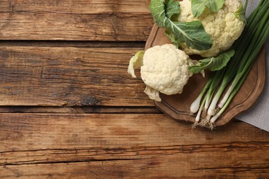 Photo of Fresh raw cauliflower cabbages and green onions on wooden table, top view. Space for text