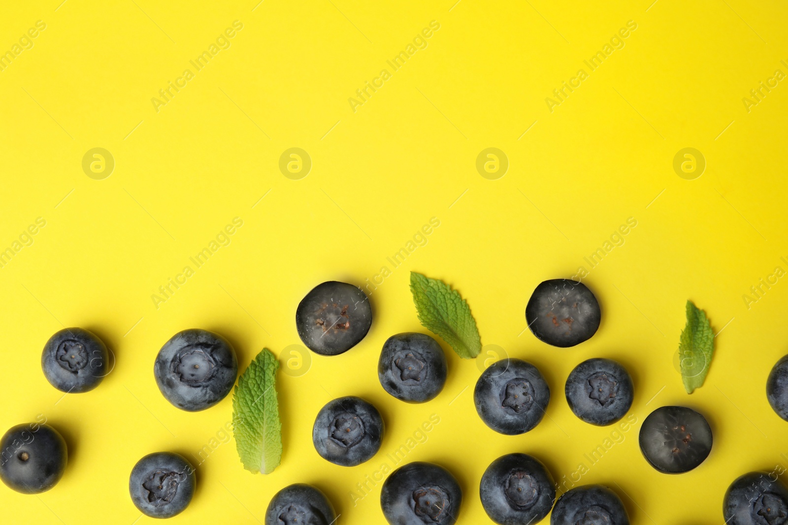 Photo of Tasty ripe blueberries and leaves on yellow background, flat lay with space for text