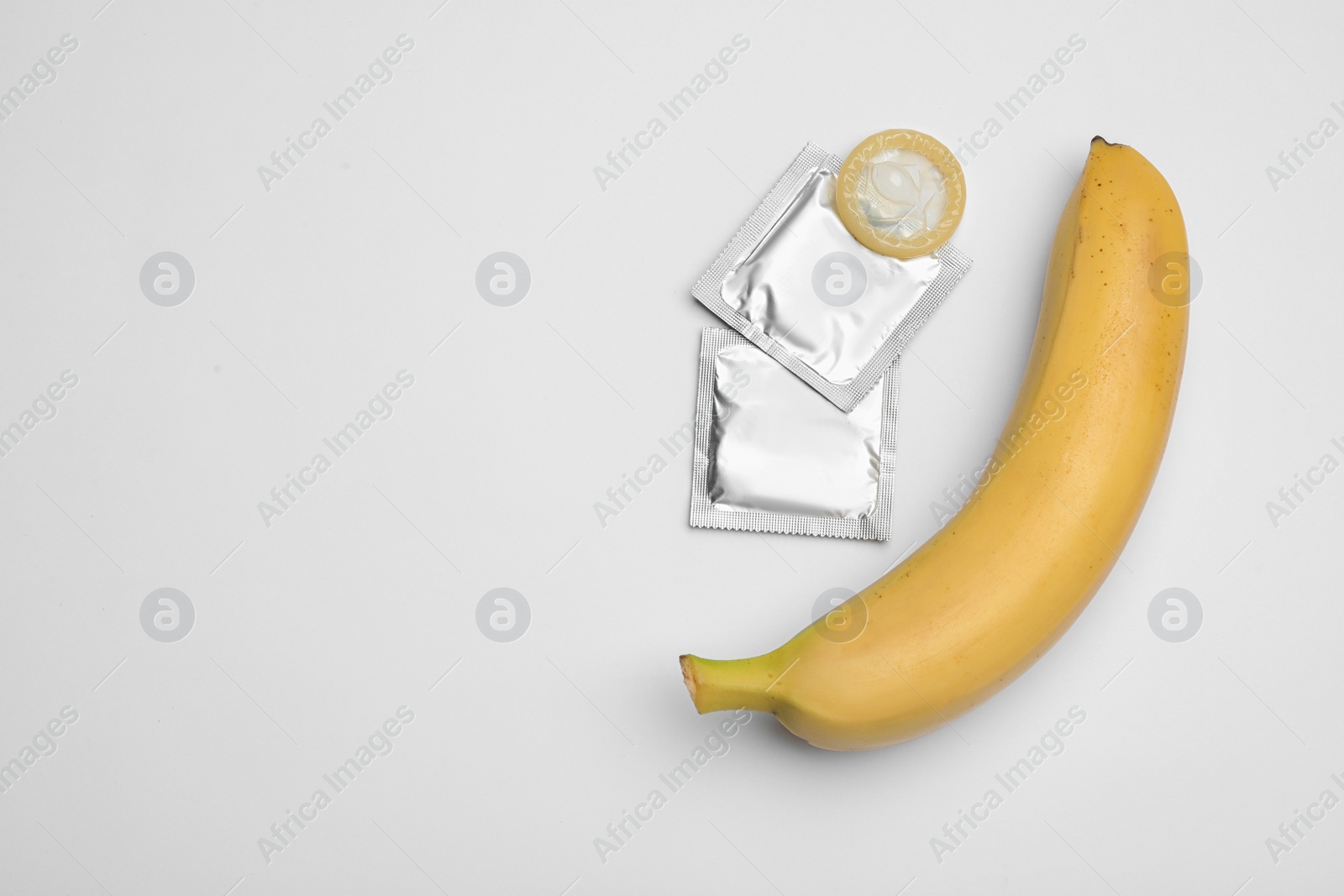 Photo of Condoms and banana on white background, top view. Safe sex