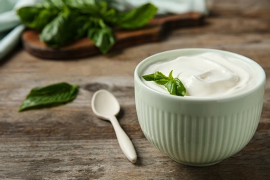 Bowl of fresh sour cream with basil and spoon on wooden table. Space for text