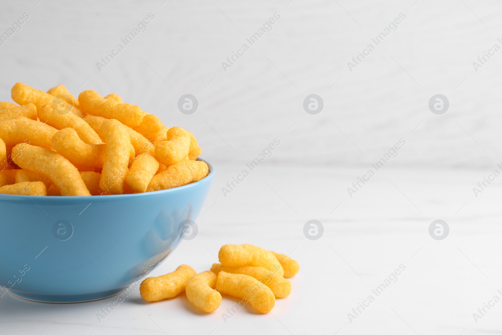 Photo of Many tasty cheesy corn puffs on white marble table, space for text