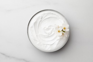 Jar of face cream and flowers on white marble table, top view